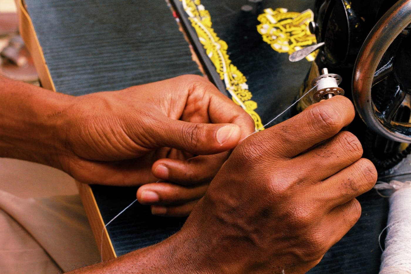 Hands threading a sewing machine in a workshop
