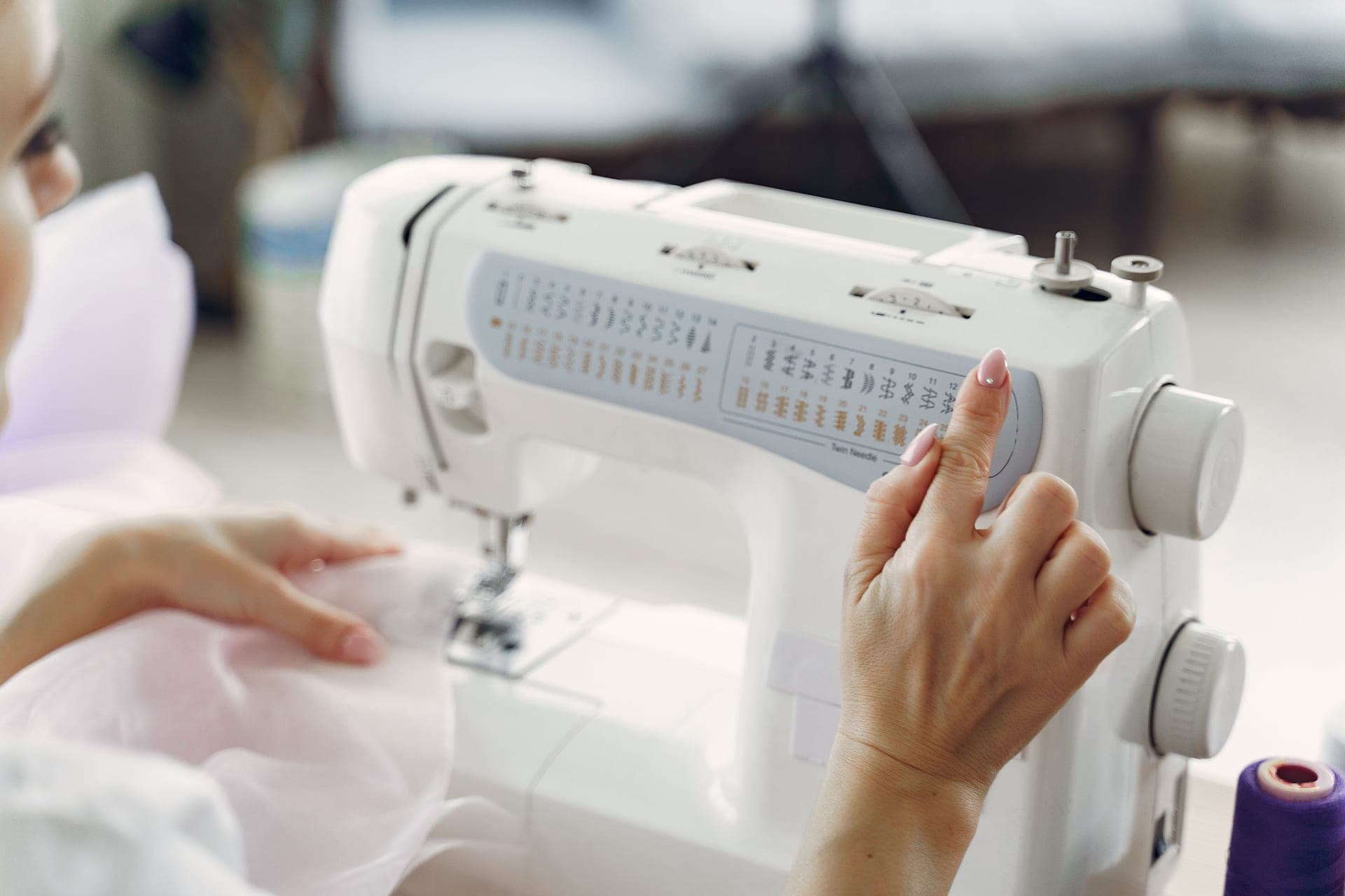 A person sewing on a white machine and adjusting its settings