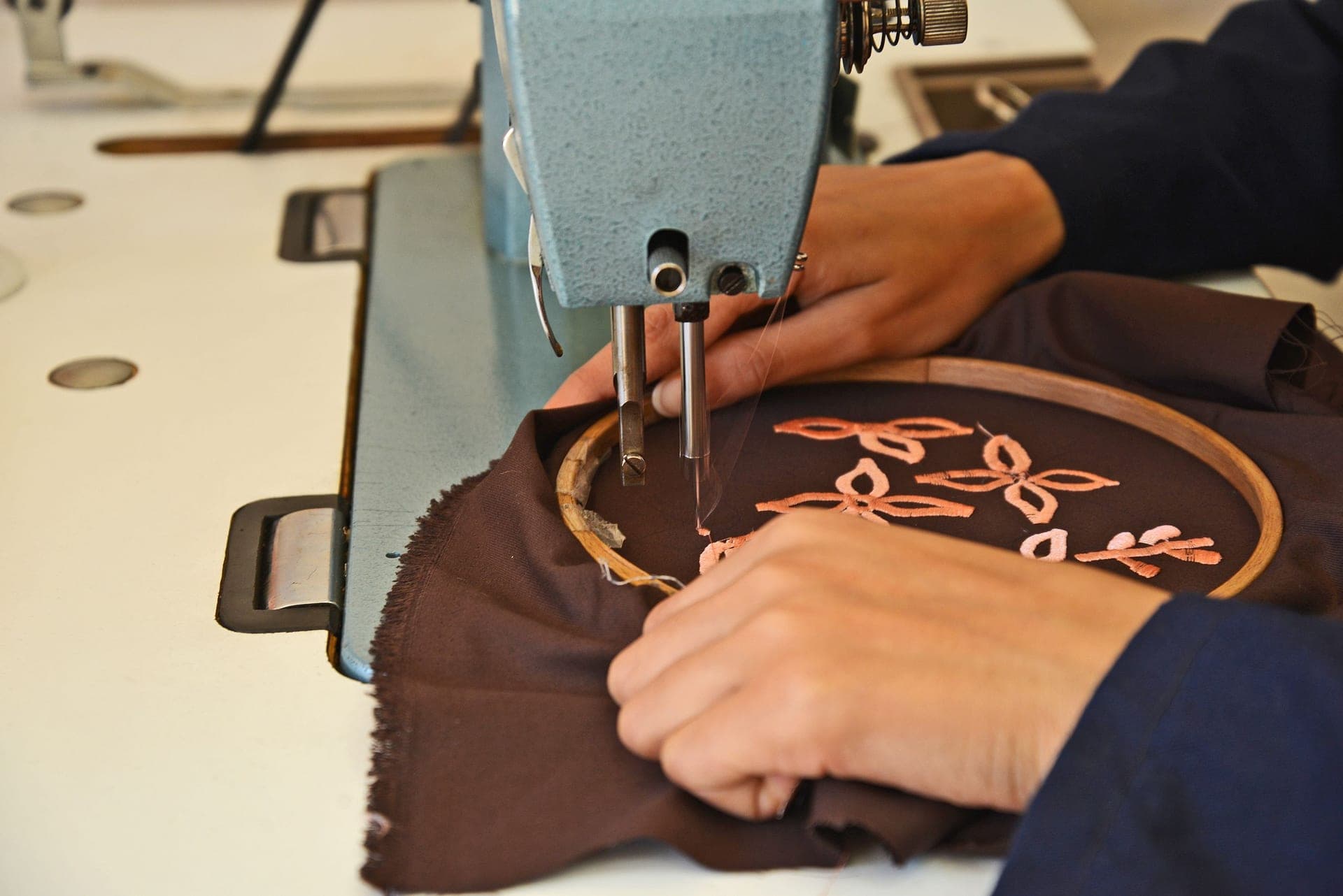 Close view of hands guiding fabric under a machine in a workshop