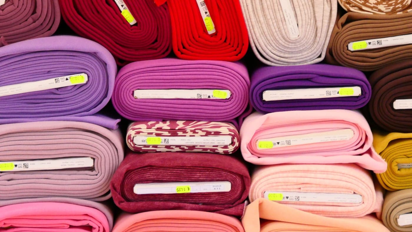 Rolls of fabric in various colors stacked at a market stall