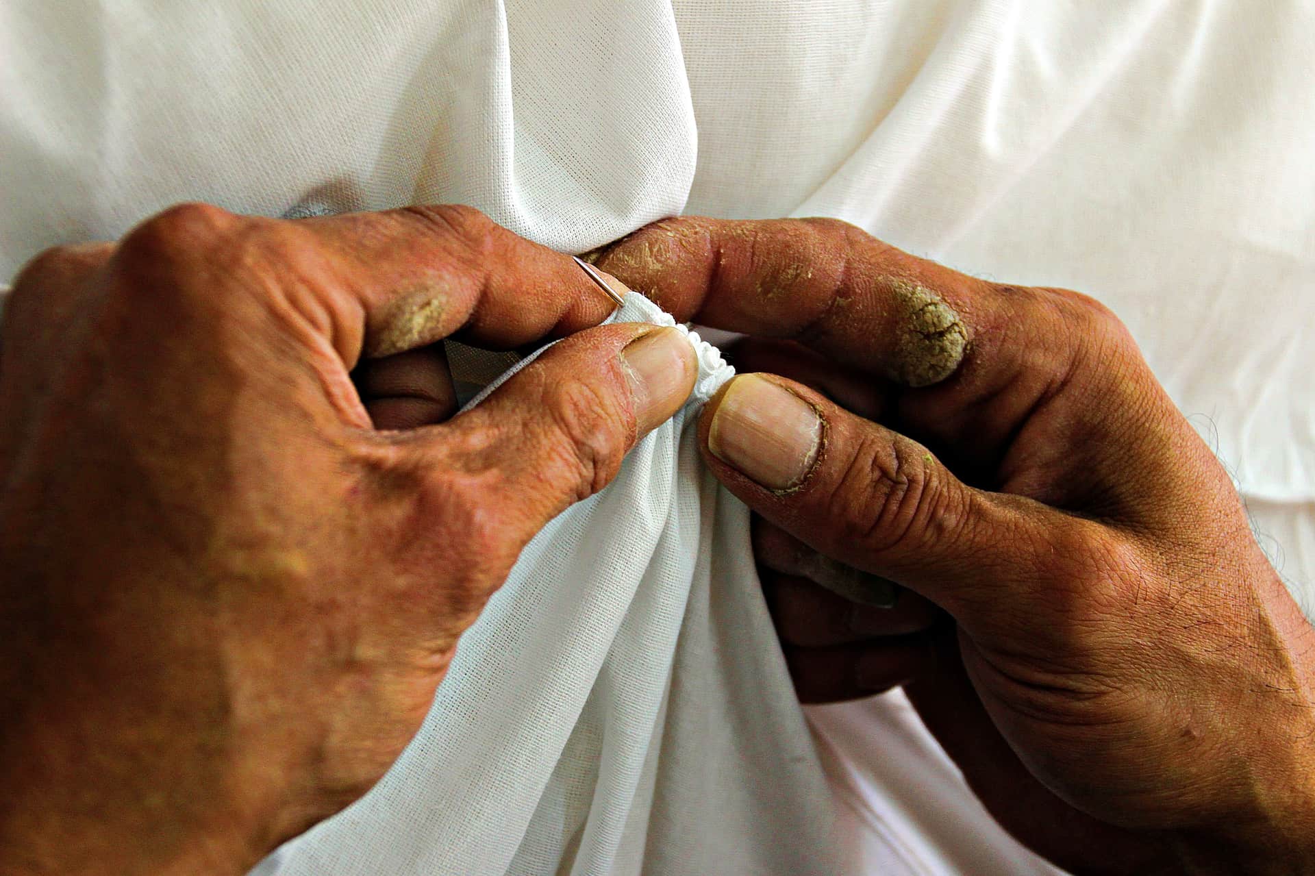 Close view of hands sewing white fabric with a needle