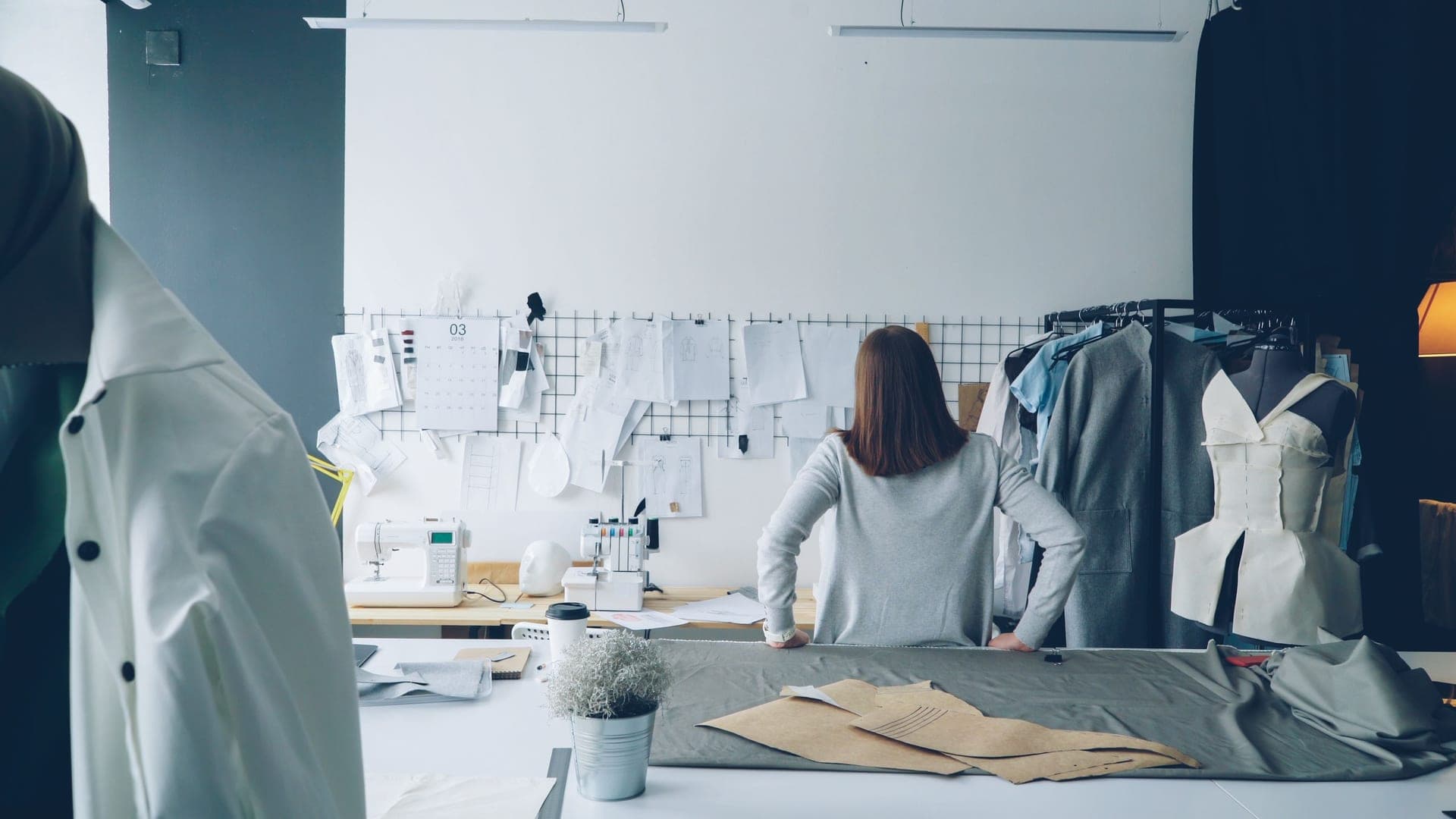 A garment maker in a studio surrounded by patterns and finished pieces