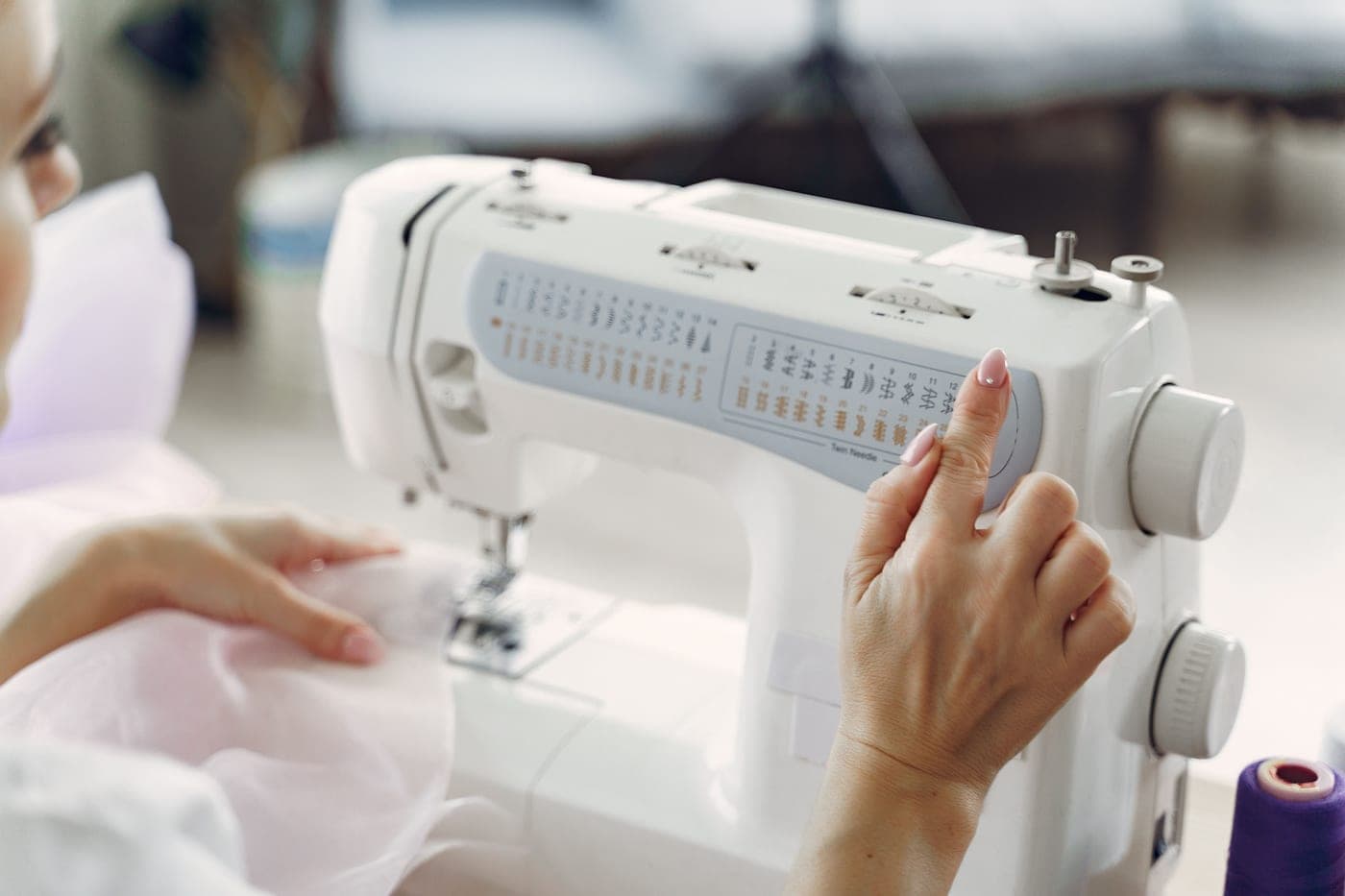 A person operating the controls of a white sewing machine
