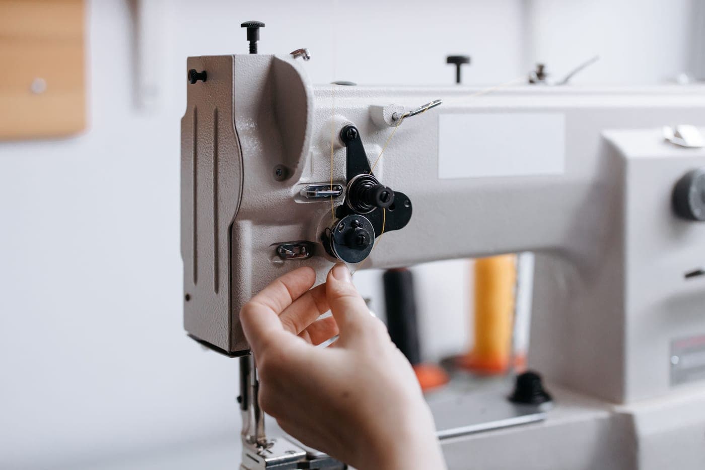 A hand working on a sewing machine with a small metal tool