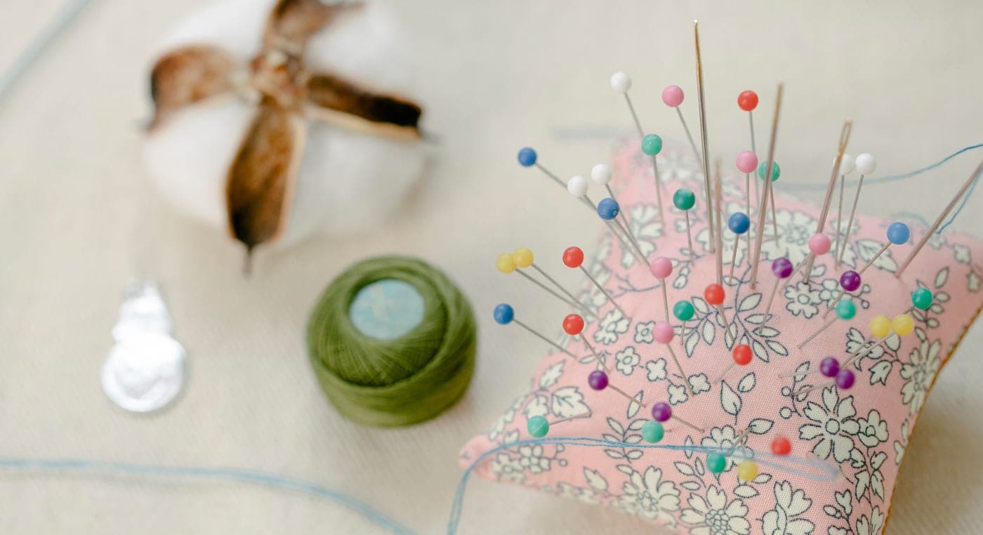 Pins in a small pincushion beside a spool of thread